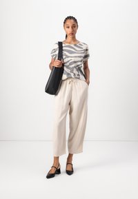 Haut à manches courtes gris et blanc à motif zèbre, pantalon crème fuselé, chaussures à talon noir avec lanière, et sac à épaule noir.