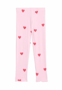 Leggings roses avec une texture côtelée, ornés de motifs de cœurs rouges dispersés et avec des ourlets effilochés au niveau de la cheville.