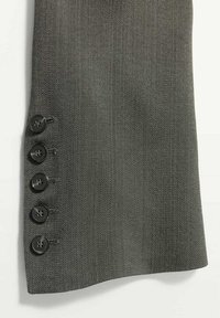Manche de costume en tissu gris avec quatre boutons noirs cousus en rangée verticale près du poignet.