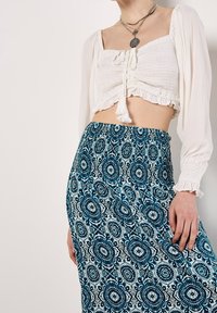 Vit kort blus med volangkant och rynkad textur, kombinerad med blå mönstrad kjol med blommönster och elastisk midjeband.