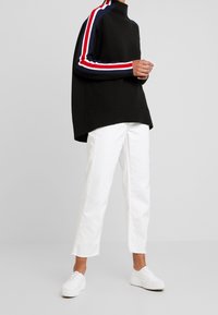 Musta huppari korkealla kauluksella, sinivalkoraidalliset hihat; yhdistetty valkoisiin lyhennettyihin farkkuihin ja valkoisiin lenkkareihin. Sileä kangaspinta.