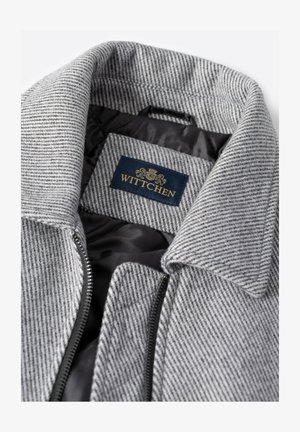 Szary płaszcz w paski z klapowanym kołnierzem, zamkiem błyskawicznym i czarną podszewką. W środku przeszyta metka marki WITTCHEN.