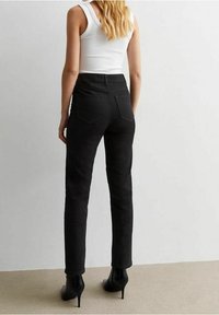 Jeans de mezclilla negra con una altura media, ajuste slim y bolsillos traseros, combinados con una camiseta sin mangas blanca y botines de tacón alto negros.