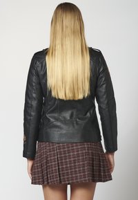 Veste de biker en cuir noir avec un design ajusté, des coutures détaillées et des broderies florales sur les manches, associée à une jupe plissée à carreaux rouges.