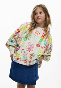 Spalvingas džemperis su įvairiais ryškiais raštais ir formomis, kreminės spalvos, laisvo kirpimo, derinamas su tamsiai mėlynomis džinsinėmis sijonais.