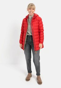 Rode pufferjack met een capuchon, ritssluiting en geribbelde manchetten. Draagt over een grijze kabelgebreide trui en grijze jeans, gecombineerd met tan kleurige enkellaarsjes.