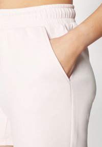 Shorts de color rosa claro confeccionados en una tela suave, con una cintura elástica y bolsillos laterales, presentando una textura lisa y un diseño sencillo.