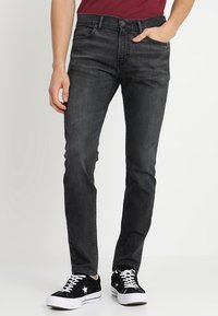 Svarta denimjeans med rak passform, femfickorsdesign och dragkedja. Bärs med svarta sneakers med vita detaljer.