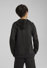 Sudadera con capucha negra de textura suave, con un corte holgado y mangas largas. El dobladillo y los puños son de canalé, con un logo en la parte inferior.
