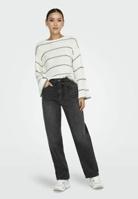Pull en tricot surdimensionné avec des rayures blanches et grises, associé à un jean noir taille haute ; modèle portant des baskets blanches.
