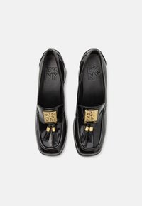 Černé lakované slip-on boty se čtveratou špičkou, s velkým zlatým logem a dekoračními střapci. Texturovaná stélka s logem.
