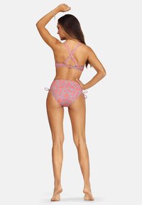 Różowy bikini w kwiaty z krzyżującymi się ramiączkami i wysokim stanem majtek. Materiał wydaje się elastyczny, podkreślony bocznymi zawiązaniami i teksturowanym wzorem.