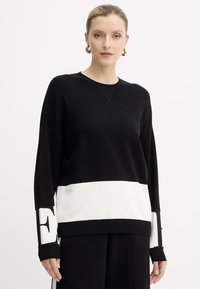 Maglione a maglia bianco e nero con scollo rotondo, vestibilità oversize, maniche lunghe, caratterizzato da dettagli a bande contrastanti e logo sulle maniche.