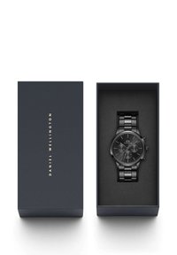 Orologio in acciaio inossidabile nero in una scatola blu navy. Cassa rotonda con accenti argentati, dettagli cronografici e design del bracciale a maglie.
