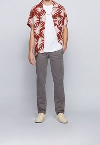 Rostfärgad skjorta med kort ärm och vitt mönster av palmblad, vit t-shirt med rund hals, grå byxor och krämfärgade sneakers. Mjukt tyg och avslappnad passform.