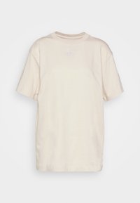 Krämfärgad bomullströja med korta ärmar, avslappnad passform och en liten vit logga vid bröstet. Slät textur och rundad halsringning.