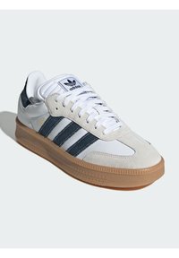 Adidas Samba sportcipők, fehér bőr felsőrésszel, szürke velúr részletekkel, kék csíkokkal és mintázott gumitalppal.