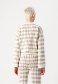 Kort, stickad tröja med ett ljust beige och vitt randigt mönster. Har långa ärmar och en ribbad nederkant, som visar en strukturerad kvalitet.