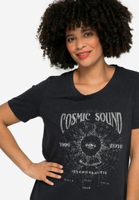 Camiseta negra de manga corta, con un diseño gráfico en blanco que muestra "SONIDO CÓSMICO" y un motivo de ojo, hecha de material de algodón.