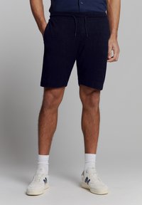 Marineblauwe katoenen shorts met een elastische tailleband, trekkingkoorddetail en zijzakken. Gecombineerd met witte sneakers en sokken.