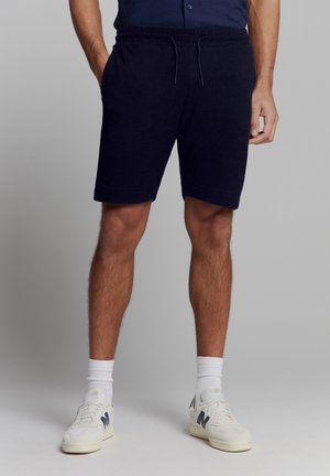 Marineblauwe katoenen shorts met een elastische tailleband, trekkingkoorddetail en zijzakken. Gecombineerd met witte sneakers en sokken.