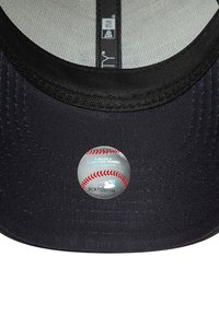 Crna bejzbol kapa od teksturirane tkanine, sa okruglim MLB logotipom naljepnicom sa dizajnom bejzbol lopte na donjoj strani okretnice.