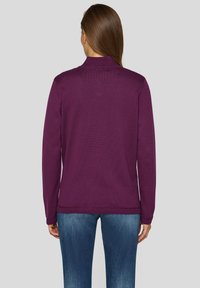 Lila gestrickter Pullover mit Stehkragen, gerippter Textur und langen Ärmeln, kombiniert mit hellblauen Jeans.