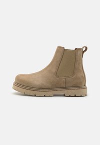 Botas Chelsea de ante marrón con paneles laterales elásticos, un lazo en la parte superior y una suela de goma texturizada para mayor agarre. Diseño de puntera redondeada.