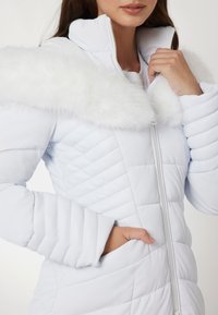 Vit pufferjacka med fuskpälskrage, med quiltat mönster, framzipper och sidofickor. Slät tygfinish.