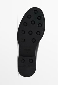 Black rubber shoe sole featuring raised circular traction patterns and a rounded toe. Textured surface with branding and size imprint.