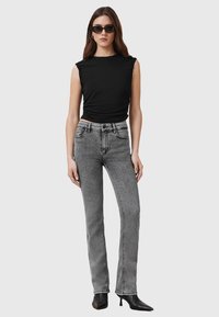 Top senza maniche nero abbinato a jeans grigi chiari a vita alta. I jeans presentano un taglio classico e una leggera sfumatura, completati da tacchi neri.