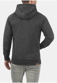Sudadera de forro polar gris oscuro con capucha ajustable, puños y dobladillo acanalados, y una pequeña etiqueta de cuero en la parte baja de la espalda. Textura suave.
