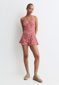 Completino floreale rosso con scollo all'uncinetto e pantaloni a shorts svasati. Realizzato in tessuto leggero, presenta un motivo a fiori bianchi e una silhouette femminile.