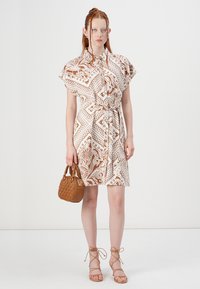 Abito camicia a righe marroni e crema con maniche corte e vita legata. Abbinato a una piccola borsa marrone e sandali con fasce.