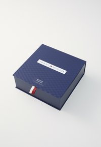 Navy blue rectangular box with a checkered pattern, featuring a white logo. A red and white ribbon accent is visible on the side.