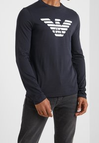 Marinblå långärmad skjorta i bomull, med en vit randig logotyp på bröstet. Enkel design, rund halsringning, mjuk textur.