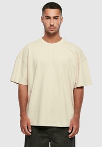 Bež oversize T-särk lühikeste varrukatega, ümmargune kaelus ja sile tekstuur. Omab vaba lõikega ja minimaalseid õmblusdetail.