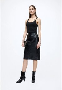 Črni zgornji del brez rokavov z detajlom na rami, kombiniran s tesno prilegajočo črno usnjeno midi krilo in sijočimi črnimi gležnjarji. Drži črni usnjeni žepni torbici.