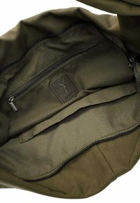 Interno di una borsa di stoffa verde oliva con una tasca con cerniera e texture liscia, decorata con una toppa in pelle e dettagli di cucitura visibili.