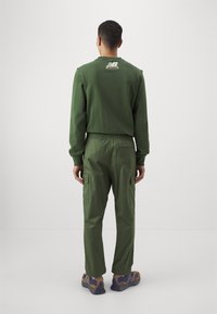 Grön sweatshirt med rund hals och logotyp bak, tillsammans med matchande gröna cargobyxor med sidofickor och elastisk midja.