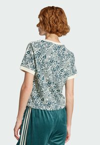 T-shirt a stampa floreale color crema con accenti verdi, caratterizzato da una vestibilità comoda, maniche corte e colletto a coste. Abbinato a pantaloni in velluto teal.