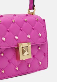 Fioletowa pikowana torebka z elementami w kolorze złotym, z wyraźną kwadratową klamrą i ozdobnymi ćwiekami. Gładka tekstura o wyraźnej, usztywnionej formie.