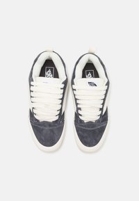 Zapatillas de ante azul oscuro con cordones y forro crema. Presentan una suela de goma blanca, superficie texturizada y etiquetas con el logotipo en la lengüeta.