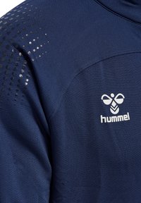 Marinblå atletisk skjorta med strukturerad tyg, prickiga mönster på axlarna och en vit 'hummel'-logotyp.