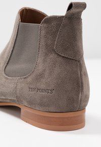 Bottine en suède gris avec des panneaux latéraux en élasthanne, bout rond et talon empilé marron. Présente le nom de la marque "TEN POINTS" embossé sur le côté.