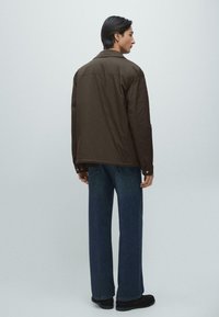 Brun lättviktsjacka med krage, kombinerad med mörkblå jeans med raka ben. Jackan har en slät textur och knappdetaljer.