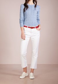 Vaaleansininen palmikkoneule, valkoiset lyhyet farkut repsottavalla helmalla, punainen vyö ja valkoiset sneakerit. Yksinkertainen muotoilu, jossa on tekstuuritettu kangas.