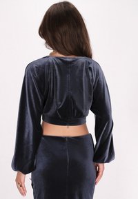 Navyblaue, kurz geschnittene Bluse mit langen, voluminösen Ärmeln. Hergestellt aus weichem, glänzendem Stoff mit einem gerafften Detail am Rücken und am Bund.
