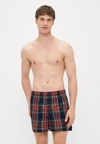 Kąpielówki w kratkę z szerokim elastycznym pasem, zdobione czerwonymi, zielonymi i żółtymi liniami na granatowym tle. Lekka tkanina, długość do kolan.