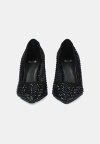 Zapatos de tacón negro con punta afilada, parte superior de tejido texturizado y panel negro plano en la parte posterior. Forro interior suave y logo embosado en la plantilla.